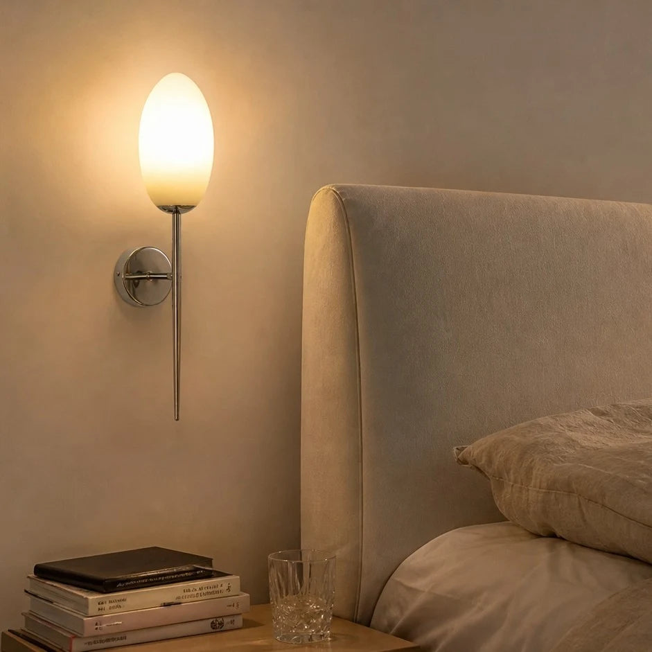 Milk glass wall sconce beside an upholstered bed